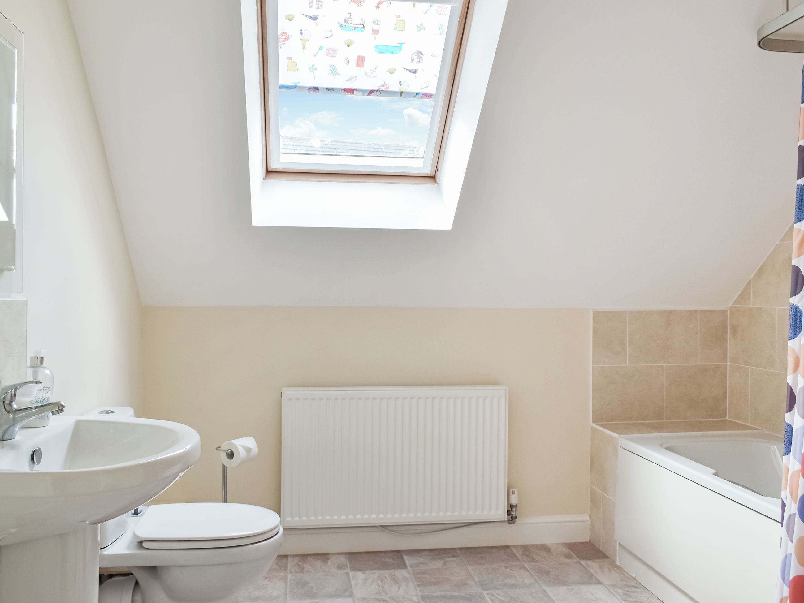 A modern bathroom with a skylight, a radiator, a bathtub, and a toilet.