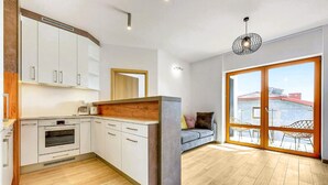 A modern kitchen with white cabinets, a built-in oven, and a wooden countertop. There is a large sliding glass door leading to an outdoor seating area with a view of the city. - 2 bedroom cozy apartment in Hel (Hel)