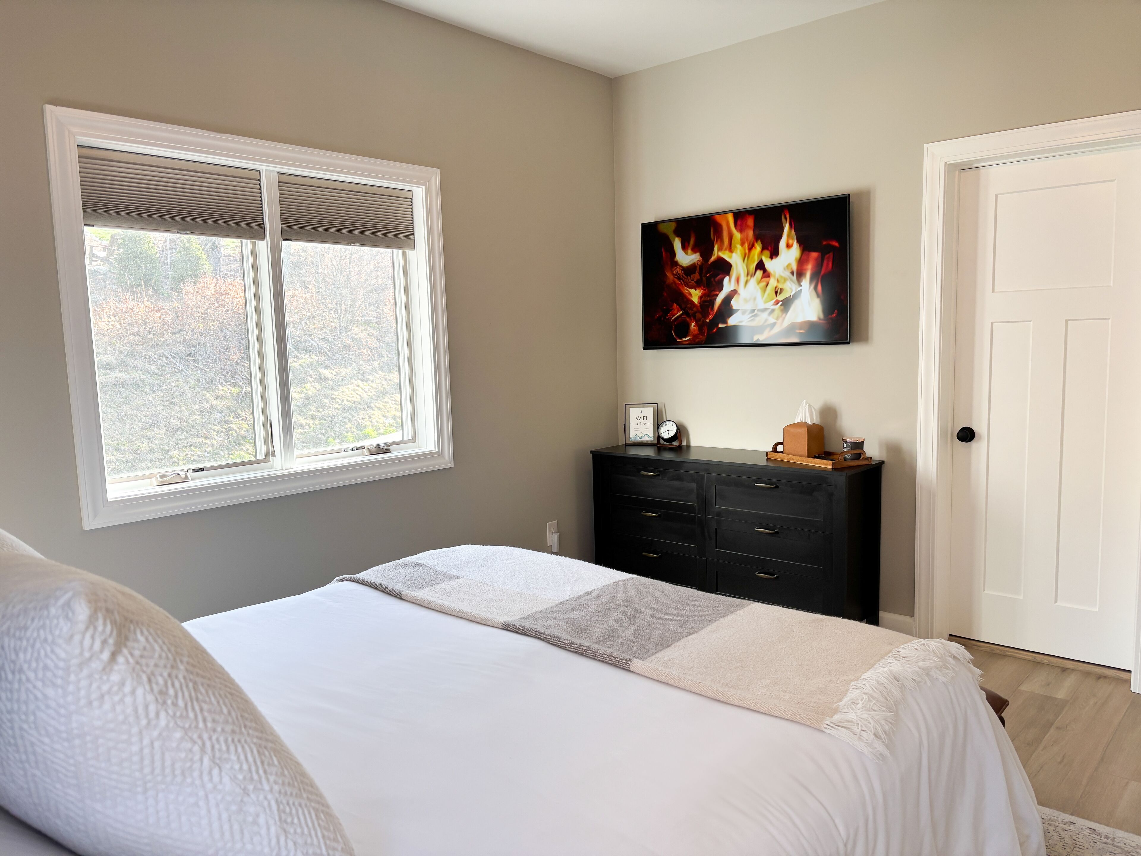A bedroom with a bed, a dresser, a painting, a window, and a door.