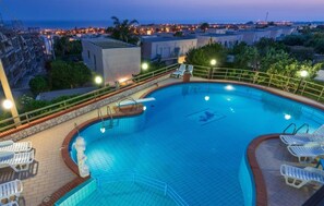A swimming pool with a curved edge, surrounded by a stone deck and a metal railing.