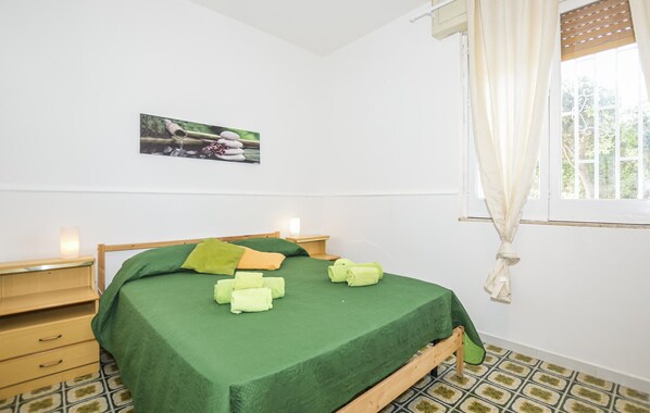 A bedroom with a green bedspread, wooden nightstands, a small bedside table, a wall-mounted picture, and a window with curtains.