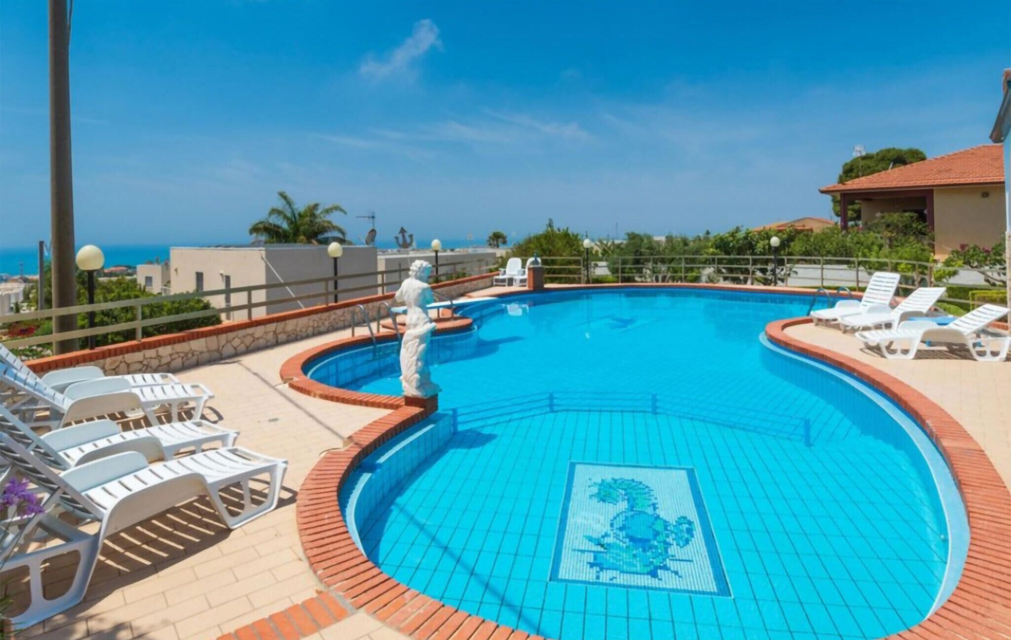 Une piscine dotée d’une terrasse carrelée, de chaises longues et d’une statue.