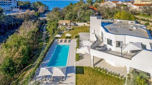 Un edificio moderno con piscina, mobiliario exterior y vistas al mar.