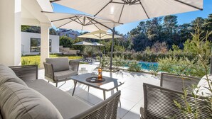 Un patio con mobiliario exterior, sombrillas y una piscina.