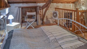 A rustic bedroom with a wooden ceiling, a metal bed frame, a small table with a lamp, and a folding chair. - Gorgeous home in Sauzet with swimming pool (Sauzet)