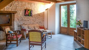 A cozy living room with a stone wall, a sofa with patterned cushions, a wooden table, and a TV on a wooden stand. - Gorgeous home in Sauzet with swimming pool (Sauzet)