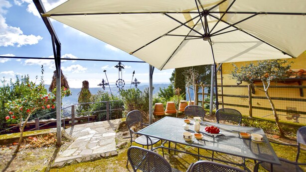A patio with a table and chairs, a large umbrella, and a view of the sea. - Cozy home in Metato with kitchen (Metato)