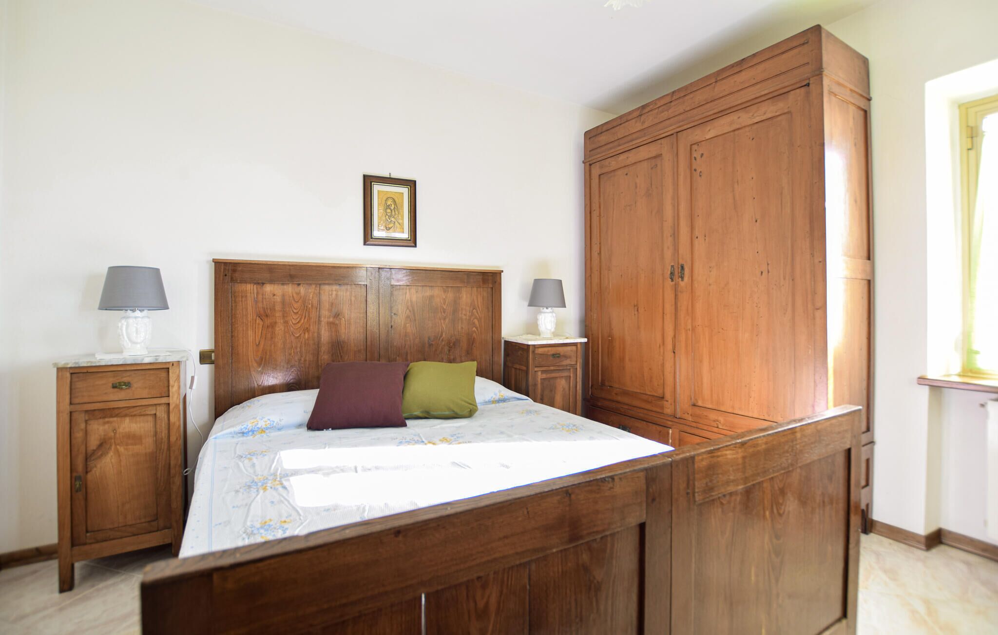 Camera da letto con un letto in legno, due comodini con lampade, un armadio grande e un quadro appeso al muro.
