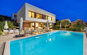 Une maison moderne à deux étages, dotée d’une piscine, d’un espace extérieur aménagé et d’un intérieur bien éclairé.