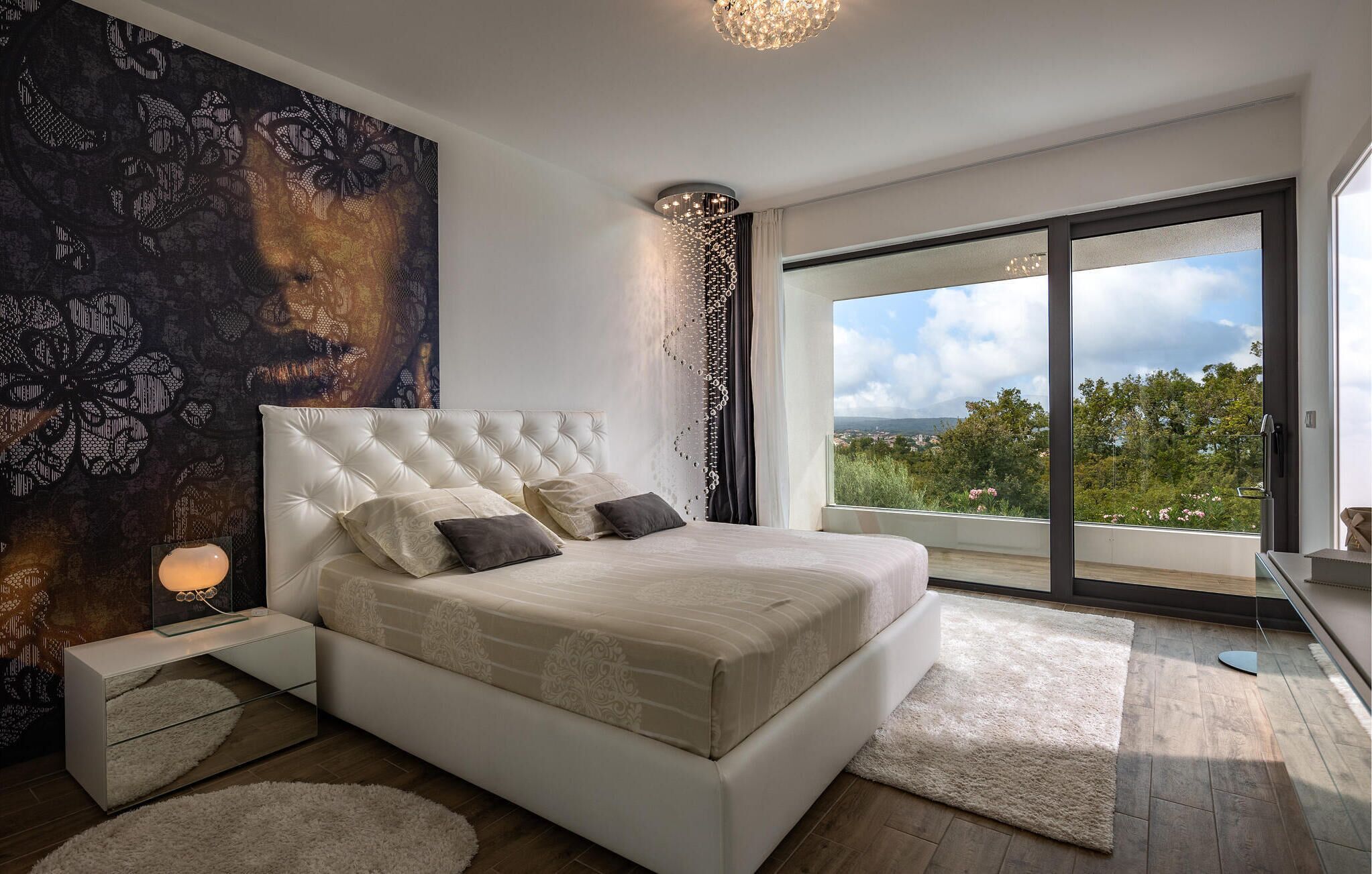 A bedroom with a large bed, a nightstand, a wall tapestry, and a view through a sliding door.