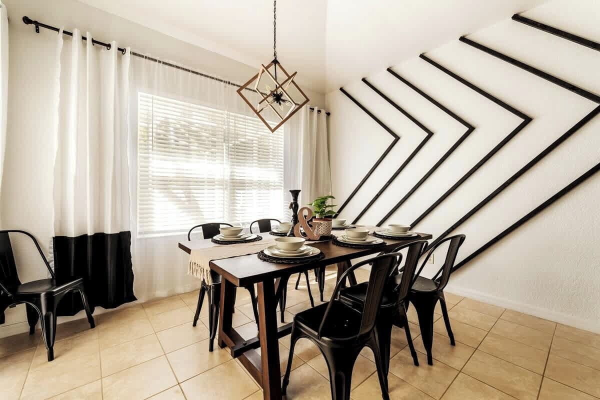 Un coin repas avec une table en bois dressée pour six personnes, des chaises noires, un luminaire suspendu et une grande œuvre d’art murale.