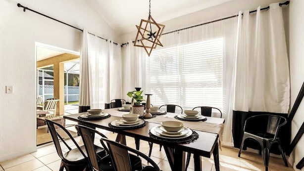A dining area with a table set for four, chairs, a hanging light fixture, and a view through the window. - Heated Pool | Game Room | Themed Rooms | Disney (Davenport)