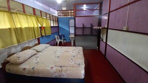 Una habitación con cama, una mesita y una silla. Hay una ventana con cortinas, y las paredes están pintadas en varios colores.