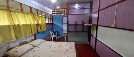 A room with a bed, a small table, and a chair. There is a window with curtains, and the walls are painted in different colors.