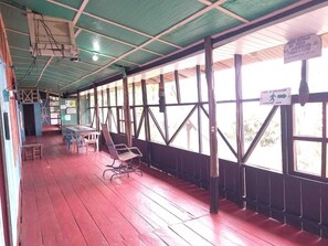 A covered outdoor area with wooden flooring, metal chairs, and tables. There are signs indicating an evacuation route and a prohibition on smoking. - hostal tachiwa-hormiga (Puerto Nariño)