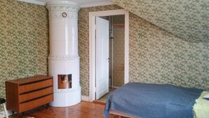 Un dormitorio con un aparador de madera, una cama con manta azul, un calentador cilíndrico blanco y una puerta que da a un armario.