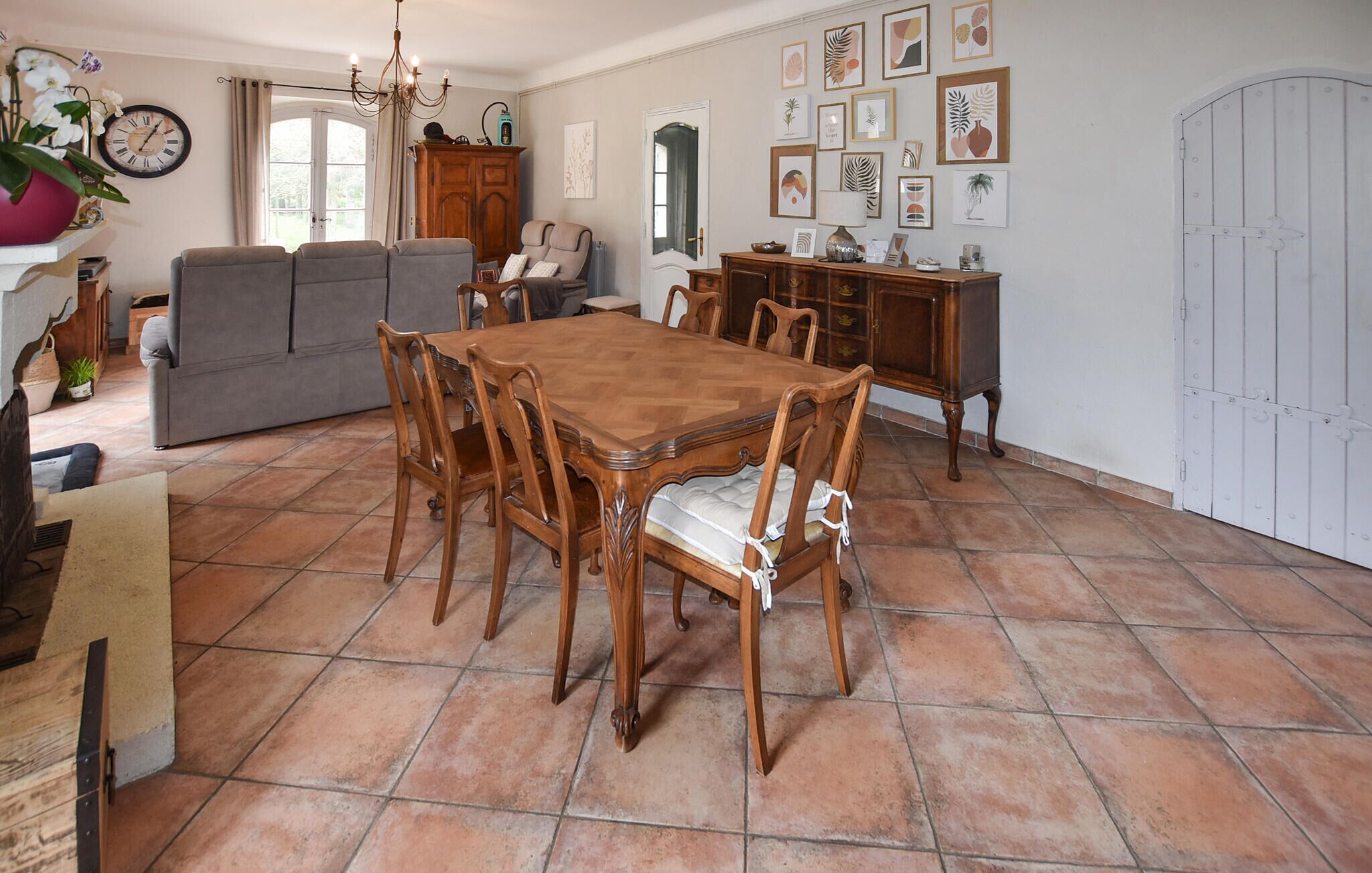 A dining area with a wooden table and chairs, a sofa, a cabinet, and a clock on the wall.