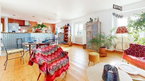 Un vaste espace de vie doté d’un plancher en bois, d’une table à manger avec des chaises, d’un canapé et d’un coin cuisine avec des meubles en bois et un réfrigérateur.