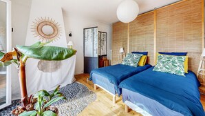 Une chambre avec deux lits, une grande plante, un miroir en forme de soleil et un mur avec des lambris en bois.