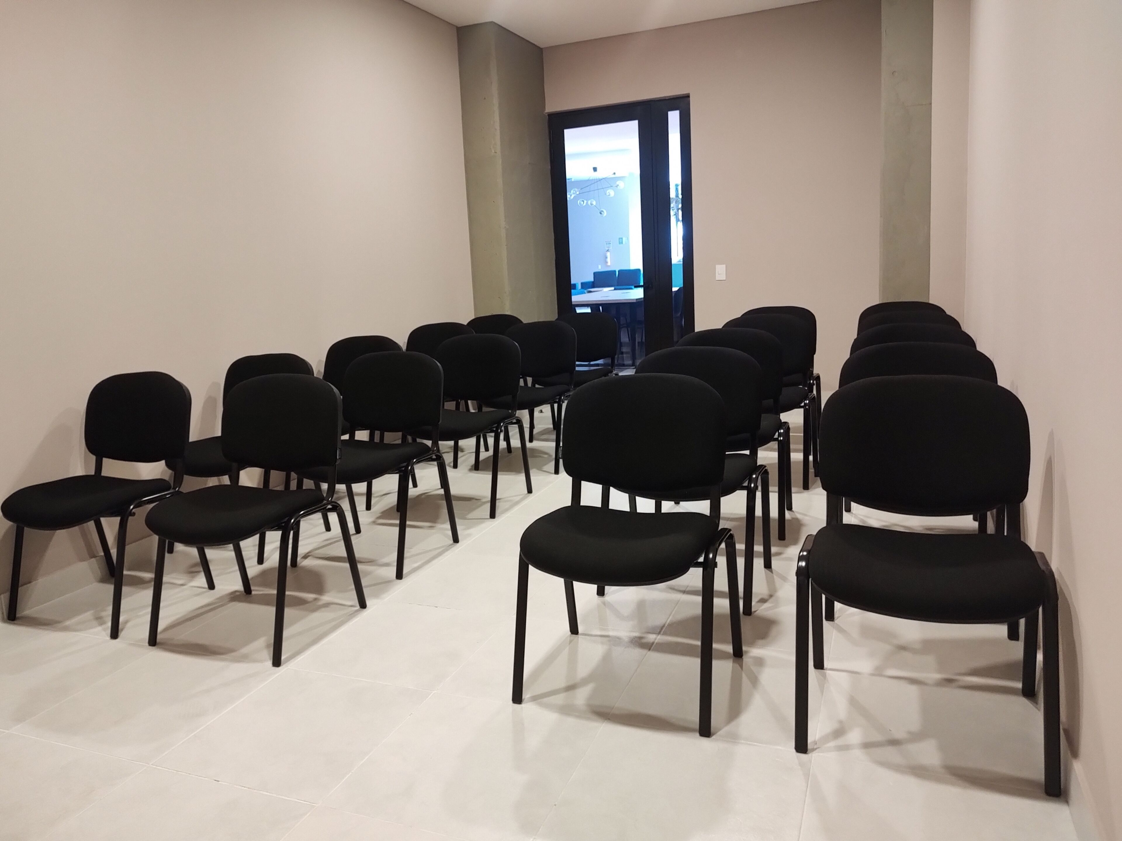 Une salle de conférence avec des rangées de chaises noires et une grande fenêtre au fond.