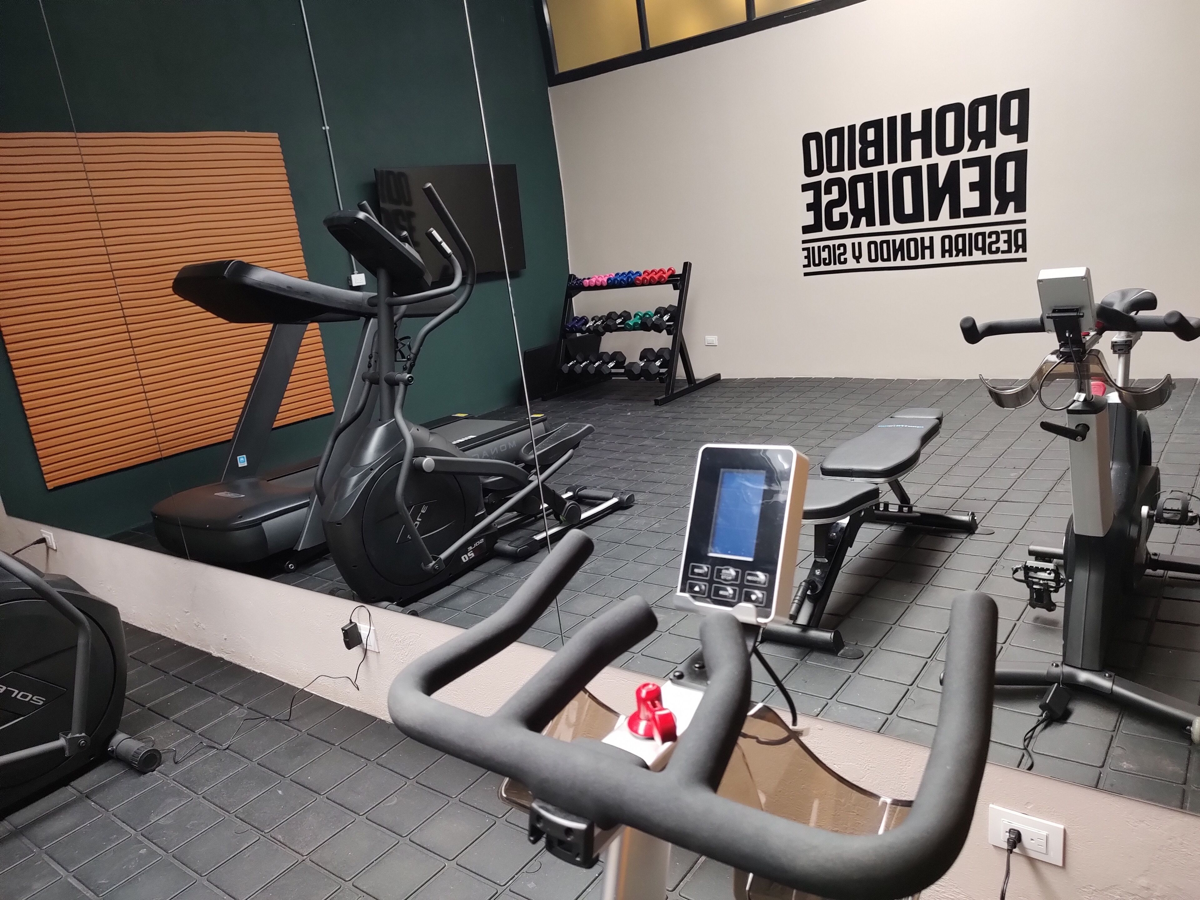 Un gimnasio con equipo de ejercicio, una pared con texto motivacional y un banco.