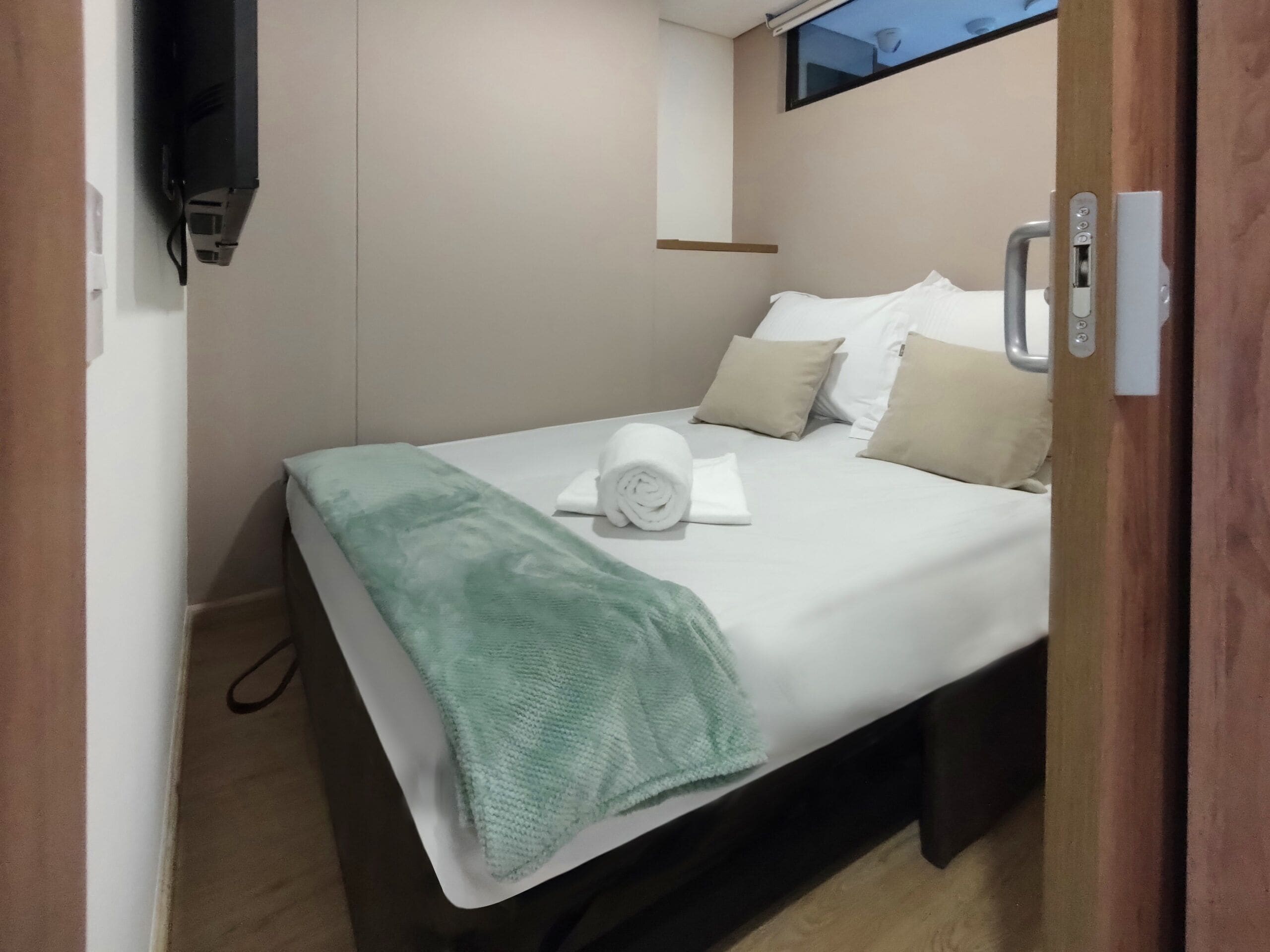 Una cama bien hecha con una manta verde, almohadas blancas y una toalla blanca enrollada.