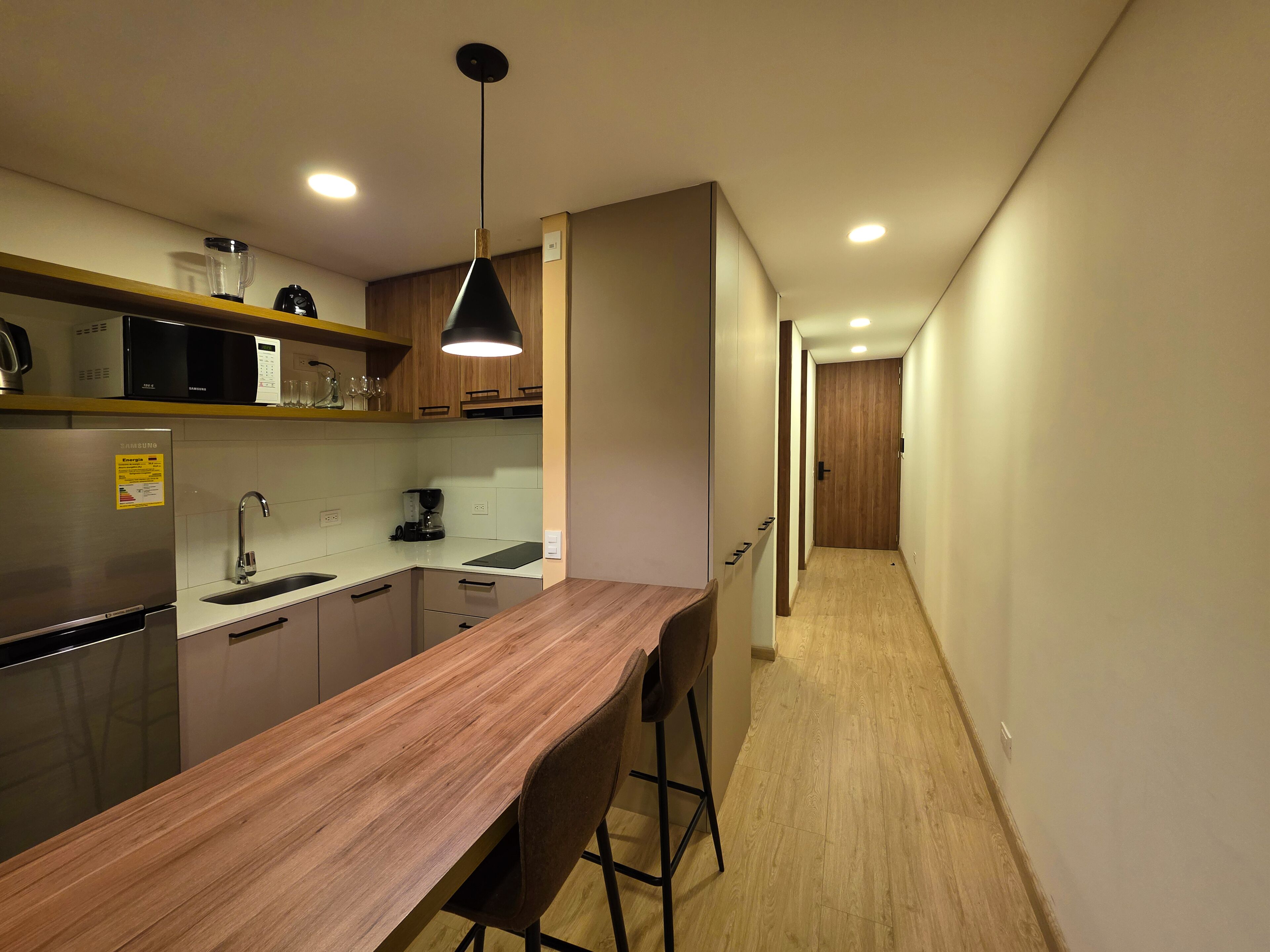 A modern kitchen with a wooden countertop, stainless steel appliances, and a pendant light.