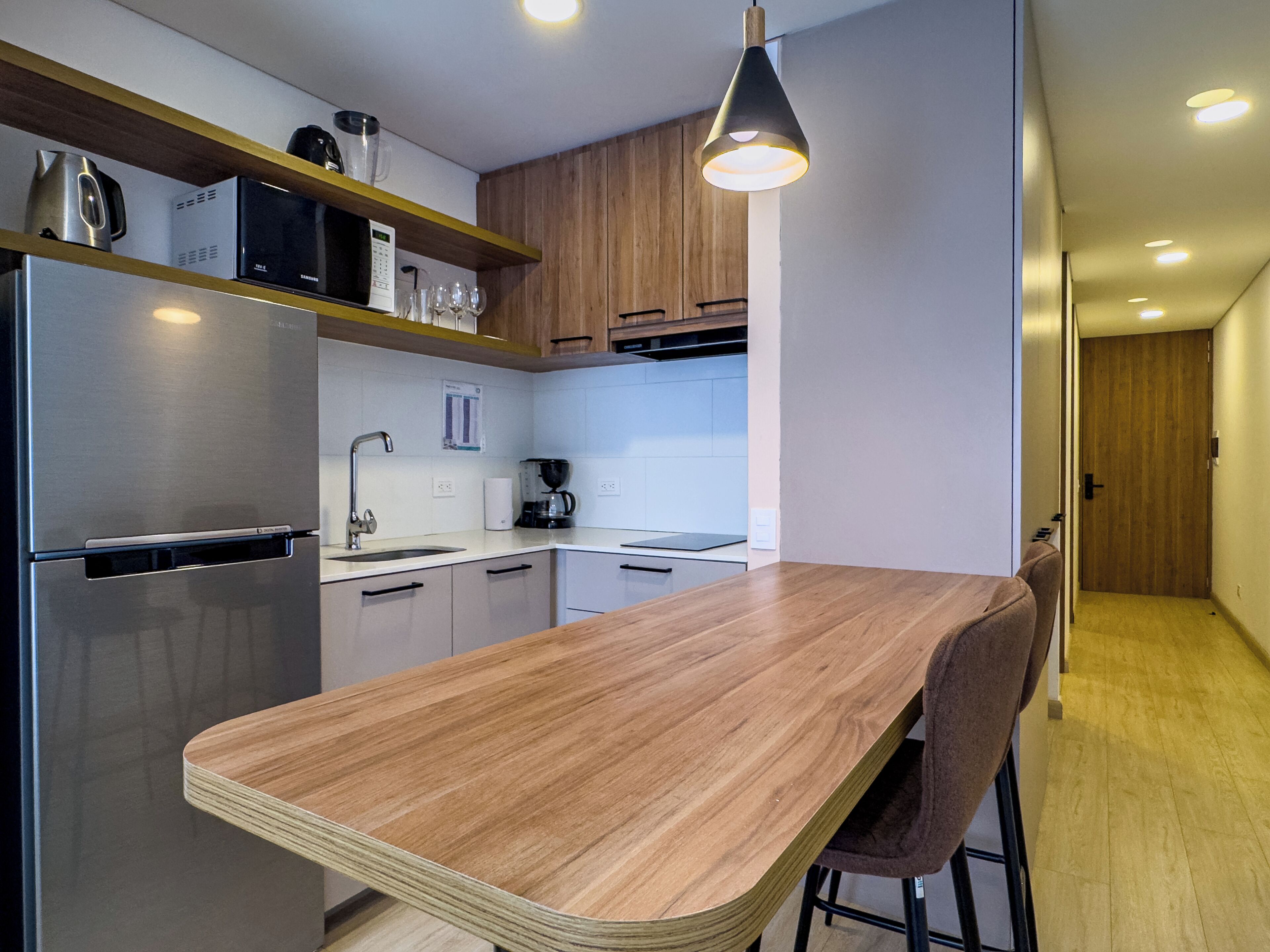 A modern kitchen with a wooden countertop, stainless steel appliances, and a hanging light fixture.