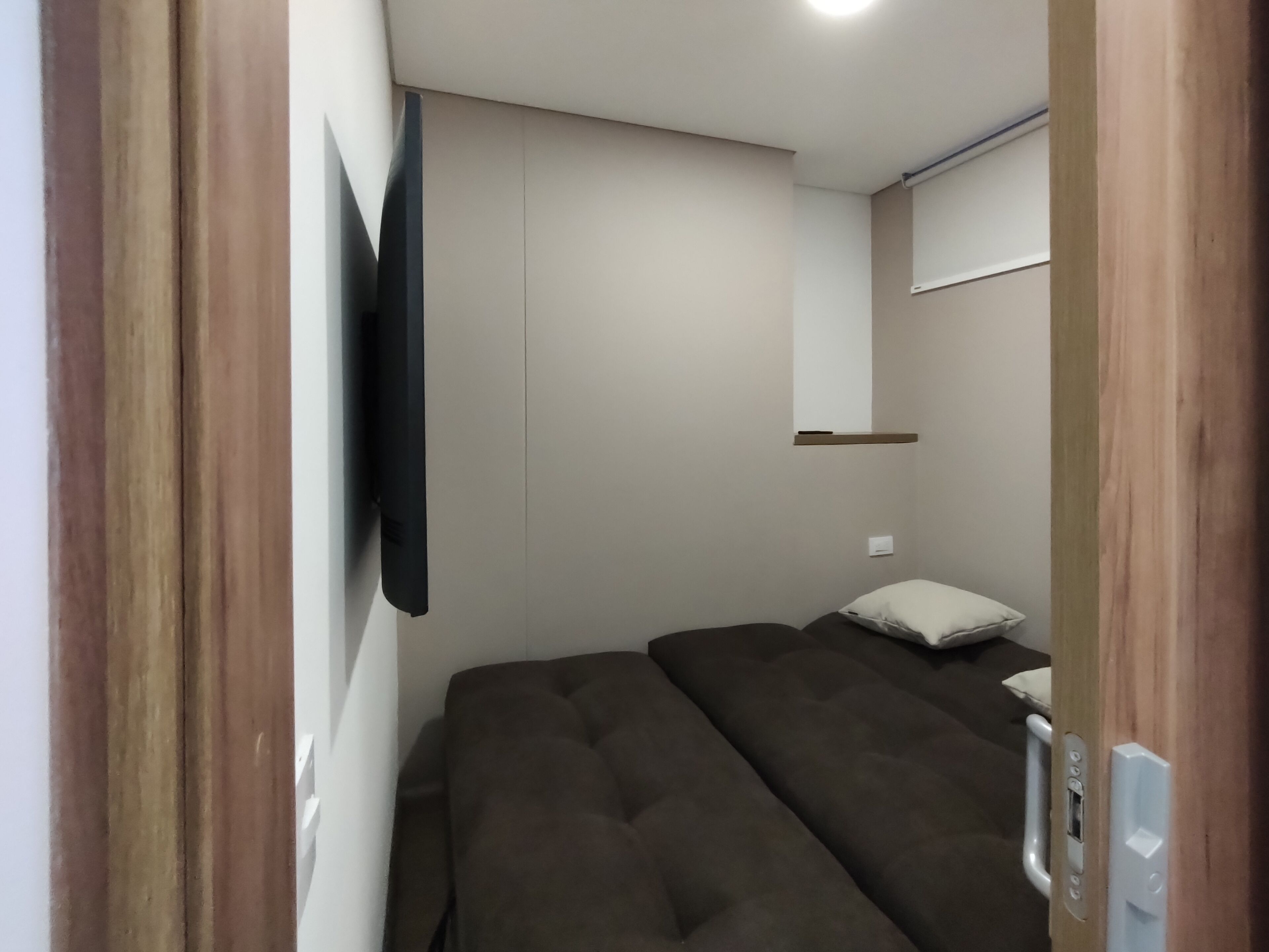 A compact room with a bed, a mounted TV, and a small shelf.