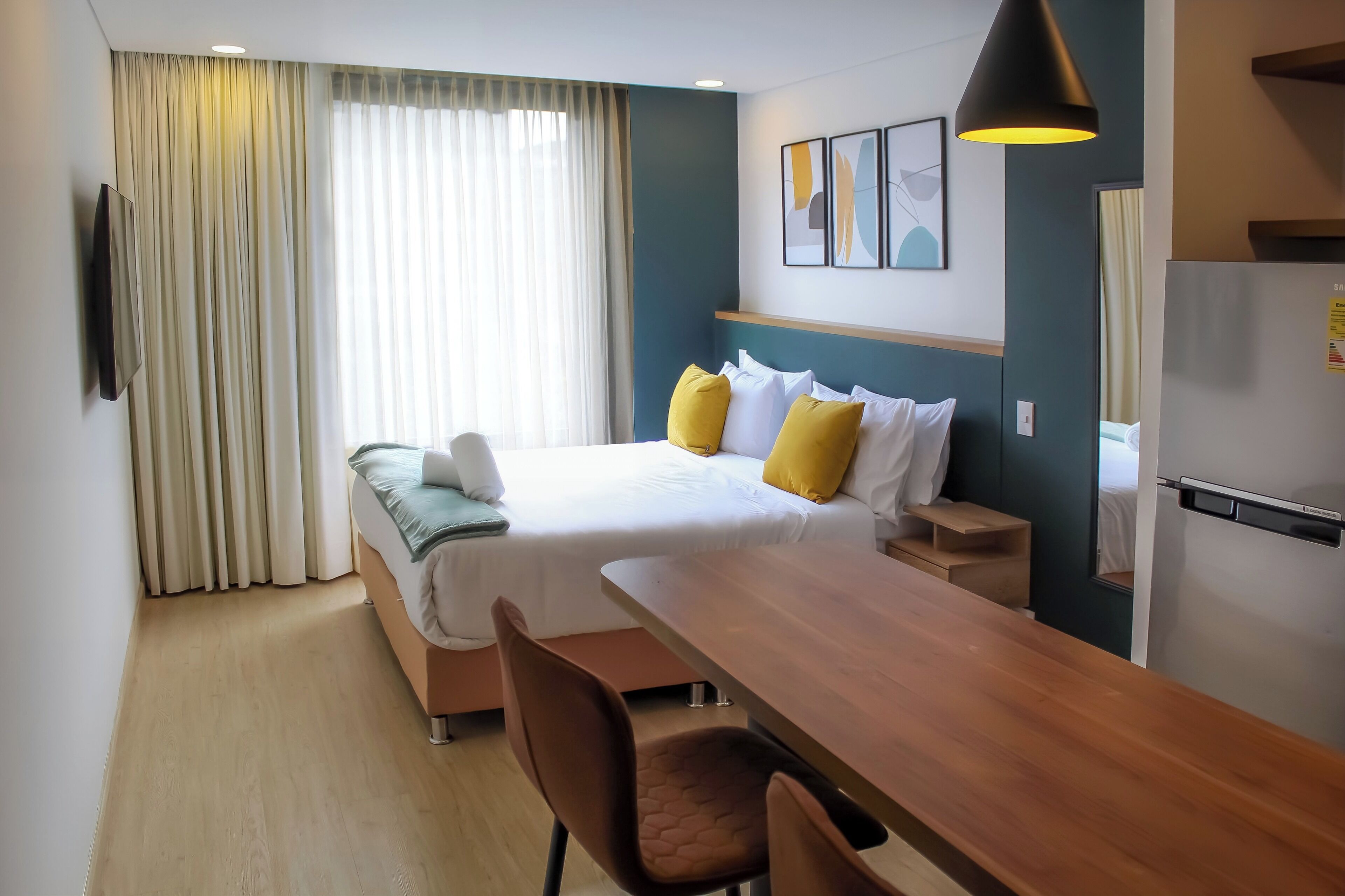A hotel room with a bed, a desk, a chair, a TV, and a refrigerator.