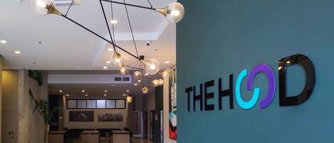 Eine moderne Hotelhalle mit einer zentralen Sitzgruppe, einer Deckenleuchte und einem Wandzeichen mit der Aufschrift "THEHOD".
