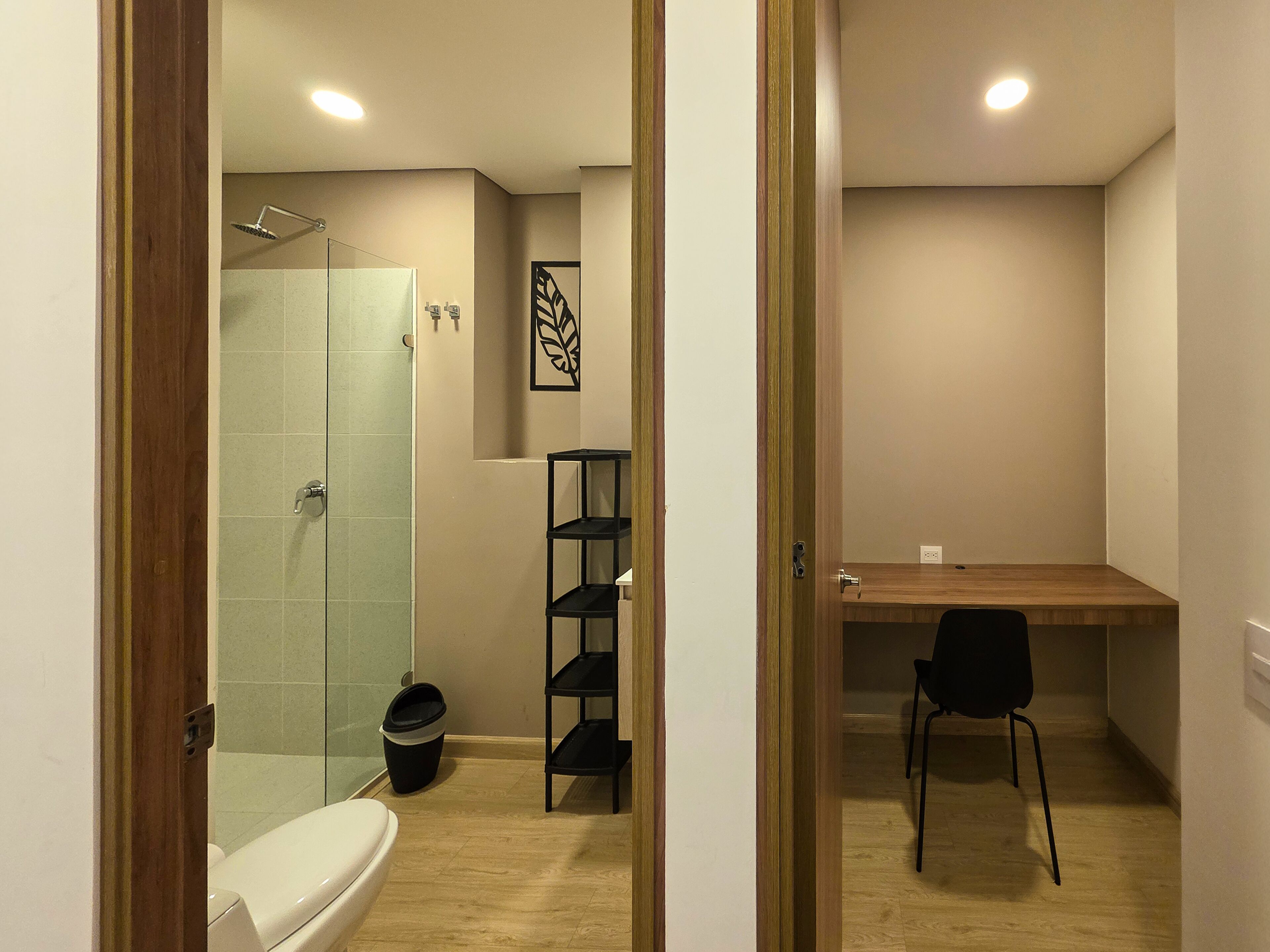 A modern bathroom with a shower, toilet, and a small desk area with a chair.