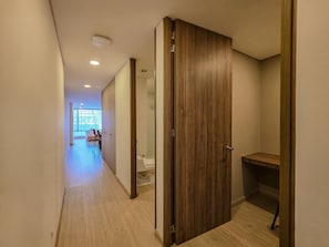 A hallway with a wooden door, a bathroom with a toilet and sink, and a seating area with chairs and a table.