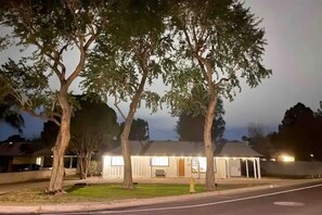 Stylish single-story home with a front porch, surrounded by mature trees and exterior lighting.
