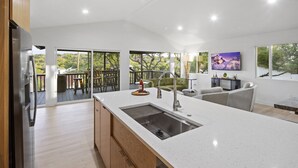 A modern kitchen with a large island, a built-in sink, and a dining area with a view of the outdoors.