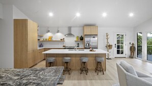 A modern kitchen with wooden cabinets, a central island with stools, and a large window.