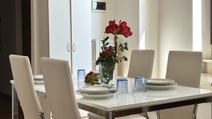 Un tavolo da pranzo con sedie bianche, un vaso con fiori rossi e bicchieri di vetro blu.