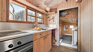 Un interior de madera con una zona de cocina, que incluye estufa, fregadero y ventanas.