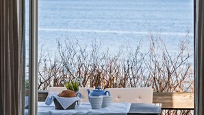 Una mesa con pan, una tetera y dos tazas, con vista al mar y ramas secas al fondo.