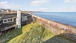 Una propiedad costera con una casa de madera, un patio con césped y una cerca de madera con vista al mar.