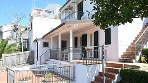 Ein weißes Gebäude mit einer überdachten Veranda, Außenmöbeln und einer Treppe zu einer oberen Ebene.
