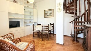 Ein Wohnzimmer mit Rattanmöbeln, einem Esstisch, einem Fernseher und einer Holztreppe.