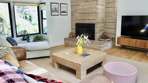 A living room with a fireplace, a sofa, a coffee table, and a television. - Designer Retreat w/ Hot Tub, Huge Backyard Oasis (Santa Cruz)