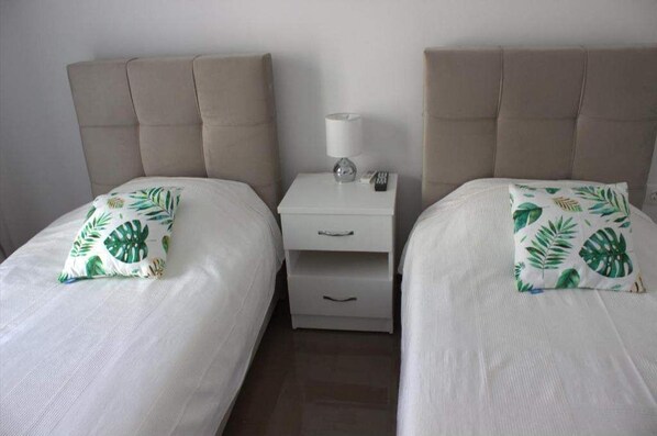 A twin room with two beds, each with a white bedspread and a green leaf-patterned pillow. There is a white nightstand between the beds with a lamp and a remote control. - Best location in the heart of Athens,under Acropolis,on touristic road Adrianou. (Athina)