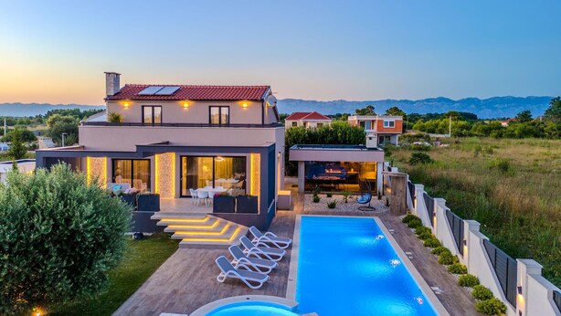 Una casa moderna de dos pisos con piscina, mobiliario exterior y vistas a la montaña.