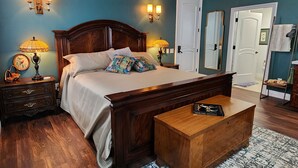 Un dormitorio con cama de madera, lámparas de noche, mesita de noche, un banco de madera y una puerta.