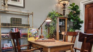 Un comedor con mesa de madera, cuatro sillas, una lámpara de araña, una estantería y una planta en maceta.