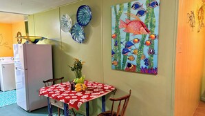 Un comedor con una mesa dispuesta para dos personas, un refrigerador y una pared decorada con un cuadro de motivos marinos.