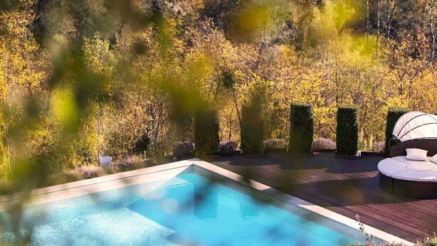 A rectangular pool with a wooden deck, surrounded by dense foliage and trees. - Tenuta Moncarlino - room Terra (Piemonte)