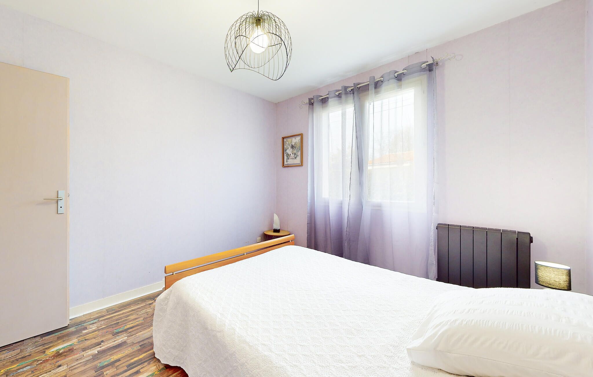 A bedroom with a bed, a bedside table, a lamp, a radiator, and a window with curtains.